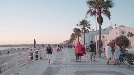 People-walk-along-Valdelagrana-Beach-in-Puerto-Santa-Maria,-Spain,-at-sunset