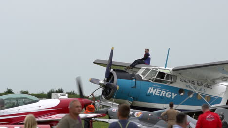 Pilot-refuels-vintage-Antonov-An-2-at-airshow,-sitting-high-on-top-wing-of-the-bi-plane-while-aerobatic-ariplanes-taxi-past-the-airplane-at-Gdynia-Aerobaltic-Airshow