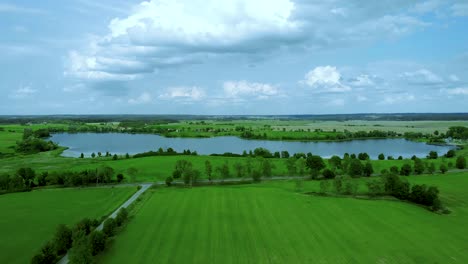 Luftaufnahmen-über-See,-Schöner-Tag-In-Der-Nähe-Von-Grasfeld-Und-Straße-Und-Teich,-Hohe-Bäume-Und-Himmel-Mit-Wolken