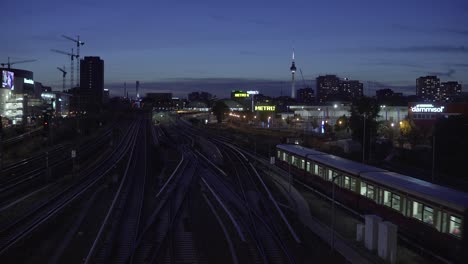 Panoramic-view-of-Berlin-at-night-with-landmark-tv-tower-and-train-on-rails