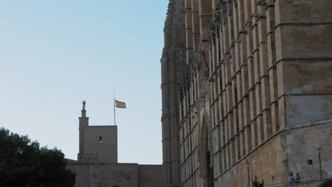 Spain-Flag-Waving-in-Air-Next-to-The-Cathedral-of-Santa-Maria-of-Palma-Exterior-on-a-Sunny-Day