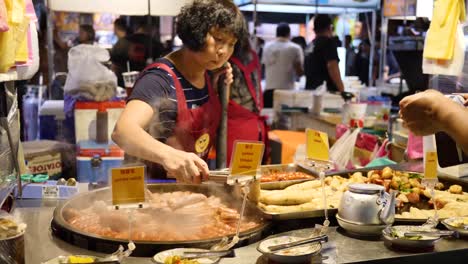 Mittlere-Aufnahme-Einer-Frau,-Die-Taiwanesisches-Essen-Von-Ihrem-Imbissstand-Auf-Einem-Nachtmarkt-Serviert