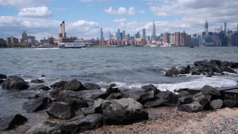 Slow-pan-across-the-New-York-City-Skyline-with-waves-breaking-on-the-beach-from-the-River
