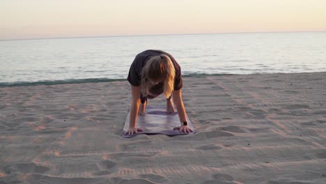 Female-stretching-on-a-beach-for-sunset,-performing-yoga-moves-n-her-yoga-mat