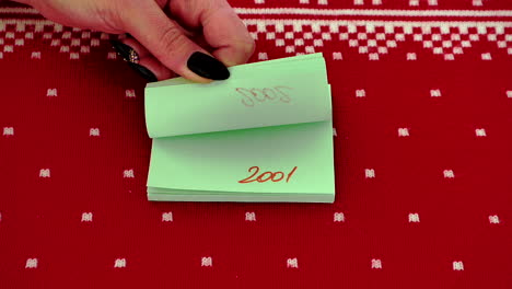 Adult-Hand-flipping-through-Post-It-notes-with-change-of-year-against-red-design-background