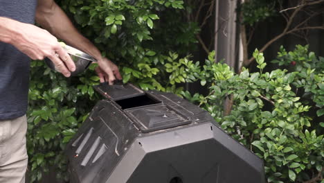 Caucasian-man-puts-food-waste-into-backyard-compost-bin,-medium-shot-fixed