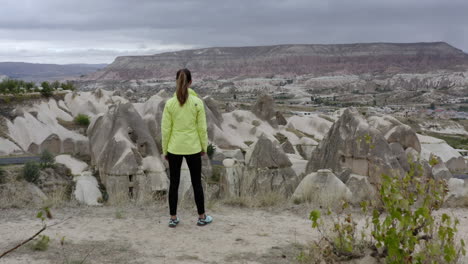 Reveal-shoot-of-woman-tourist-running-to-the-cliffs-edge-to-see-the-fairy-chimneys-in-Goreme-Turkey