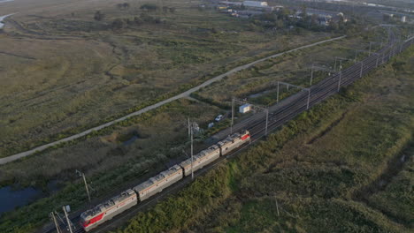 Russian-railway-train-locomotives-move-through-green-fields-with-mountains-in-the-background-on-the-sunset,-Russian-Federation