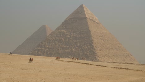 Alte-ägyptische-Pyramiden-In-Der-Nähe-Von-Kairo-Mit-Kamelen,-Die-über-Den-Heißen-Wüstensand-Laufen