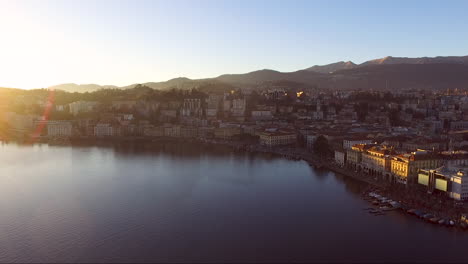 A-drone-view-of-a-city-surrounded-by-mountains,-next-to-a-lake,-during-a-sunset-in-autumn