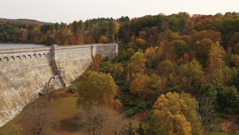 aerial-pedestal-shot-downward-over-the-orange-colored-tree-tops-in-autumn-with-the-dam's-297-foot-wall-in-view