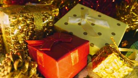 Close-up,-Stack-of-gift-boxes-under-Christmas-tree-with-lights-flashing-in-background,-hand-held