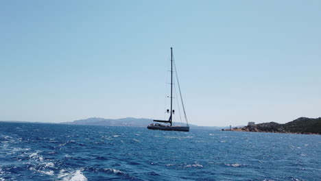Wide-shot-of-a-sailing-boat-cruise-in-front-of-the-island-through-the-blue-sea,-Sardina,-italy