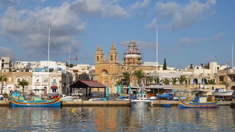 Marsaxlokk,-Malta---October-14,-2019:-Port-and-skyline-of-Marsaxlokk-traditional-fishing-village-in-Malta,-an-island-in-the-Mediterranean-Sea