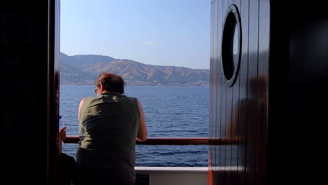 Ansicht-Von-Hinten-Erwachsener-Mann-Aus-Der-Innenkabine,-Der-Sich-An-Die-Bootsreling-Lehnt,-Während-Er-Das-Ionische-Meer-überquert