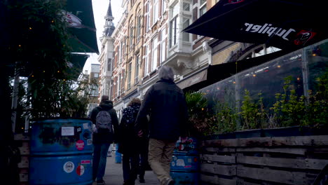 Five-people-walking-past-cafes-and-shops-Nieuwe-Binnenweg,-Rotterdam,-Netherlands-with-plants-growing-from-rubbish-bins