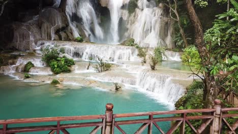 Male-Tourist-Walking-Over-Bridge-Under-Natural-Pools-of-Kuang-Si-Falls,-Laos
