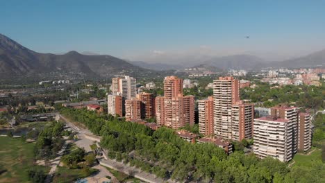 Aerial-reveal-of-Luxury-apartment-buildings-while-a-helicopter-cross-the-skyline-at-Bicentenario-Park,-Santiago-de-Chile,-4K