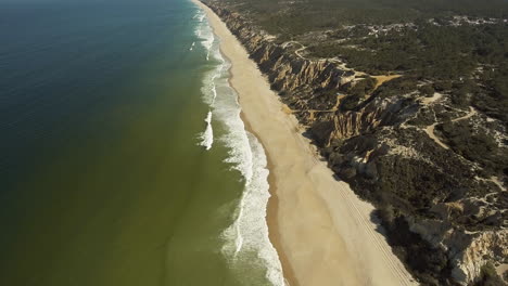 Wunderschöne-Landschaft-Aus-Felsigem-Wald-Und-Wellen,-Die-An-Der-Sandigen-Sturmküste-Spritzen,-In-Der-Nähe-Des-Campingplatzes-Praia-Da-Gale-In-Portugal---Luftdrohnenaufnahme