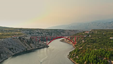 wide-aerial-shot-of-a-big-red-bridge-on-a-beautiful-mountain-scenery-on-sunset,-camera-descending