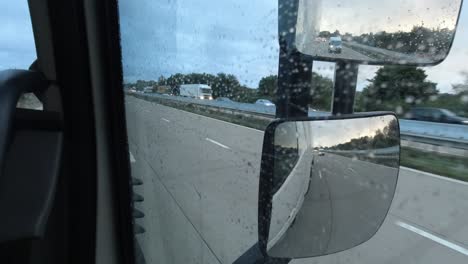 Konzeptaufnahme,-Die-Die-Sicht-Eines-LKW-Fahrers-Auf-Einen-Außenspiegel-Mit-Herannahendem-Verkehr-Im-Regen-Auf-Der-Autobahn-Zeigt