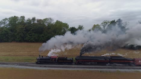 Aerial-Side-View-of-a-Two-Steam-Locomotives-Double-Heading-a-Freight-Train-Puffing-Along-with-Black-Smoke-and-Steam