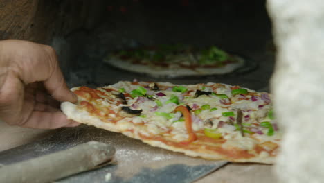 Hand-puts-pizza-on-paddle-and-pushes-into-brick-oven,-close-up,-60fps