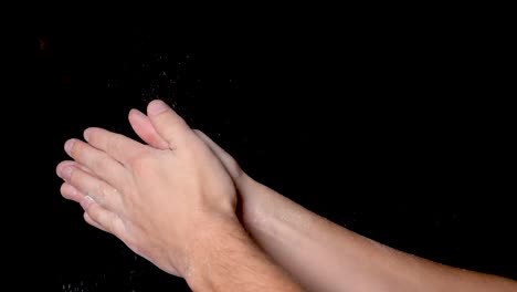 An-athlete-preparing-for-workout-by-rubbing,-chalking-and-clapping-his-hands-for-evenly-distributing-the-chalk-powder,-isolated-on-black-background
