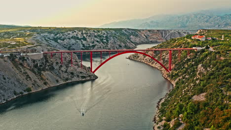 wide-aerial-shot-of-a-big-red-bridge-on-a-beautiful-mountain-scenery-on-sunset,-camera-moving-sideways