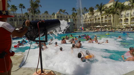 A-guy-with-a-tall-hat-spraying-people-at-a-foam-party,-in-a-resort-pool,-in-Cabo-San-Lucas,-Mexico