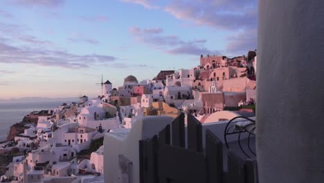 Reveal-shot-of-the-village-of-Oia-with-the-famous-windmill-and-the-ocean-in-the-background-during-sunset,-Santorini