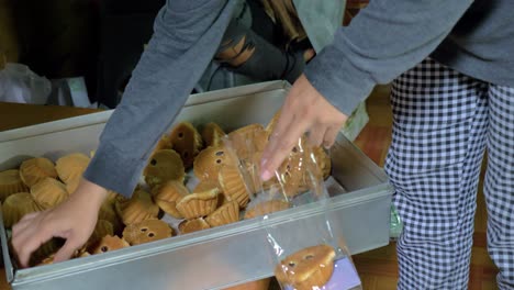 Die-Hände-Der-Frau-Legen-Traditionelle-Thailändische-Cupcakes-Mit-Rosinen-In-Eine-Durchsichtige-Plastiktüte