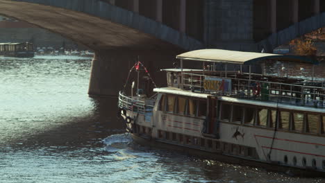 Large-tour-boat-travels-Vltava-River-under-Prague-bridge,-slow-motion