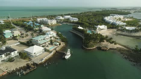 Aerial-View-of-Resort-and-Neighborhood-on-Knight's-Key-in-Marathon-Florida-With-Fishing-Boat-and-Palm-Trees-Blowing-in-Wind-and-Ocean-in-Background-Tracking-Forward-Pan-Up