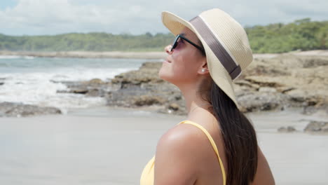 Primer-Plano-De-Una-Hermosa-Niña-Costarricense-Sonriendo-Con-Gafas-De-Sol-Y-Sombrero-Disfrutando-Del-Mar-En-La-Playa-De-Tambor,-Costa-Rica