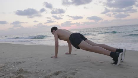 Fit-handsome-man-exercising-on-beach-at-sunset-performing-push-ups