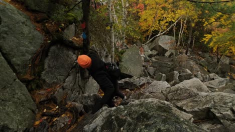 Young-Man-Climbs-Huge-Rocks-in-Fall-Leaf-Colors,-Slow-motion-Handheld-Pan