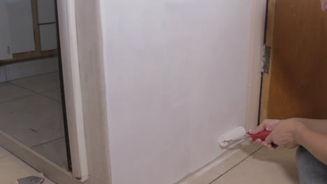 locked-off-wide-angle-of-woman-painting-primer-on-a-cupboard-with-a-roller