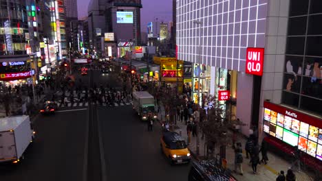 Busy-street-with-purple-sky-in-Shinjuku-Tokyo-city,-road-center-with-people-walking-and-crossing,-night-scene,-4K-panning-left
