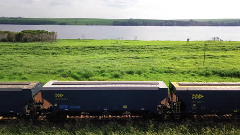 Train-waiting-to-load-grain-in-intermodal-port,-in-the-background-a-beautiful-river,-very-green-vegetation,-beautiful-landscape