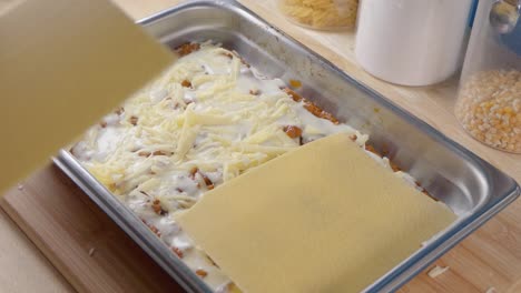 Medium-Shot-of-Adding-Pasta-Sheets-to-Cheese,-Bechamel-Sauce-and-Tomato-Sauce-in-a-Baking-Tray-for-Making-Lasagne