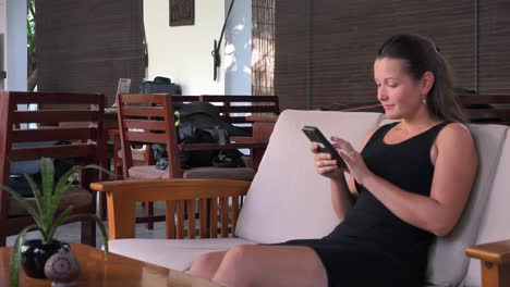 Medium-Shot-of-a-Young-Lady-Traveler-Sat-in-a-Hotel-Reception-Checking-her-Phone