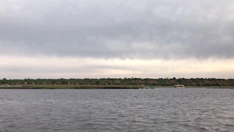 Cruising-past-sightseeing-tour-boat-on-overcast-Chobe-River,-Africa