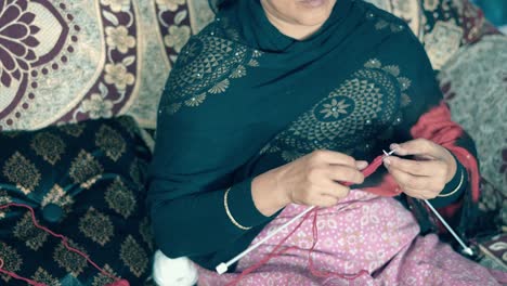 Indian-woman-sitting-on-bed-and-knitting-with-red-wool