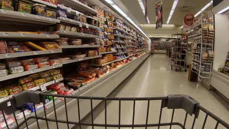 POV-from-the-shopping-cart-while-going-down-a-refrigerated-grocery-store-aisle-with-bacon,-sausage,-cold-cuts-and-cheese