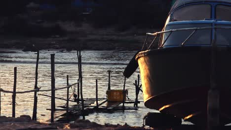 Close-Shot-of-the-Front-of-a-Boat-on-the-Shore-in-the-Evening-Time-With-Boats-Going-Past-Behind-it-on-the-Lake,-in-Front-of-Shoreline