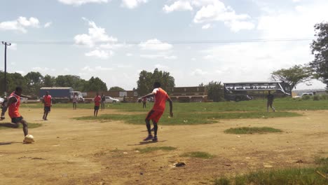 Eine-Zeitlupenaufnahme-Afrikanischer-Jugendlicher,-Die-Auf-Einem-Unbefestigten-Platz-Am-Straßenrand-Fußball-Spielen