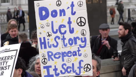 A-person-on-a-protest-opposing-war-with-Iran-holds-a-placard-covered-in-peace-symbols-and-blue-writing-that-reads,-“Don’t-let-history-repeat-itself”