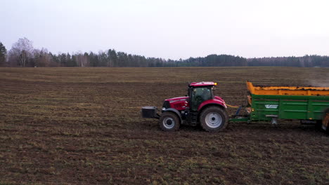 AERIAL:-Close-Up-and-Locked-Down-Shot-of-Red-Tractor-Spreading-Manure-on-the-Field-in-Evening,-Manure-Intended-for-Land-Fertilizer-Before-Planting-the-Crop