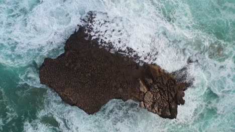 Ocean-rock-battered-by-waves-in-Praia-Do-Tonel,-near-Cape-Sagres-Portugal,-Aerial-top-view-lowering-reveal-shot